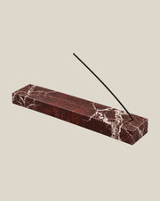 Three-quarter view of LINEA Incense Holder in Rosso Levante marble, with an unlit incense stick.