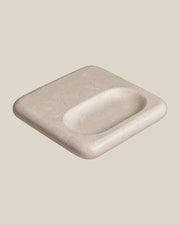 PAD Tray in beige natural stone, three-quarter view showing its rounded square shape and offset oval recess.