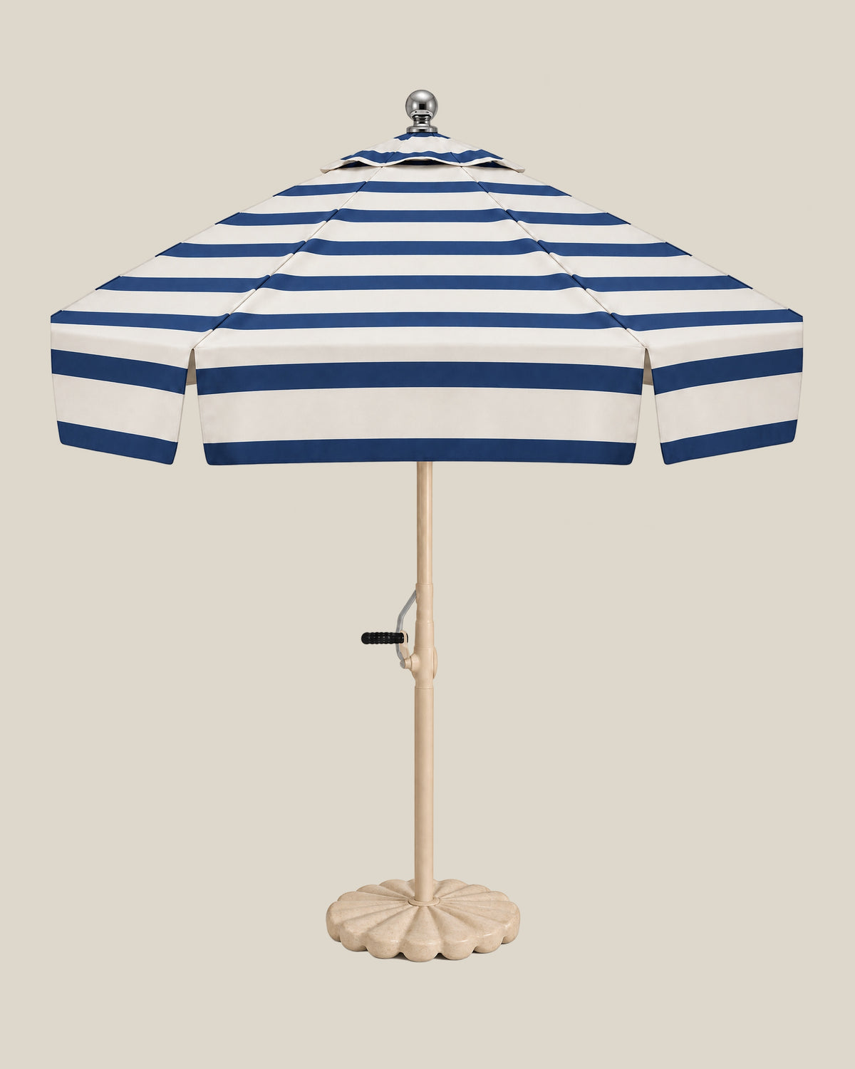 Riviera umbrella with navy stripes across its ivory canopy and tiered top, beige pole and scalloped travertine base on bone